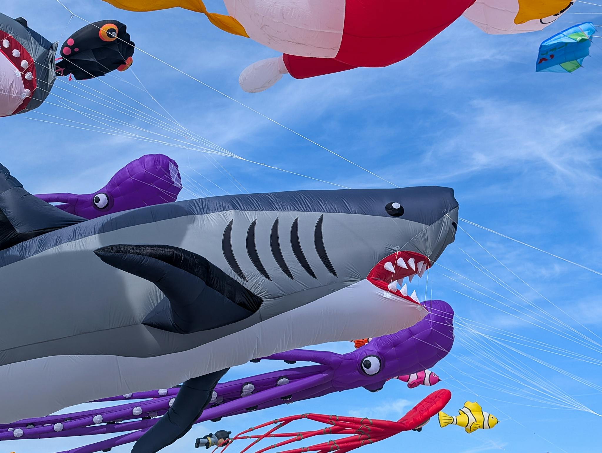Bright inflatable kites in shark and octopus shapes flying in a clear blue sky during a festival in Denmark.