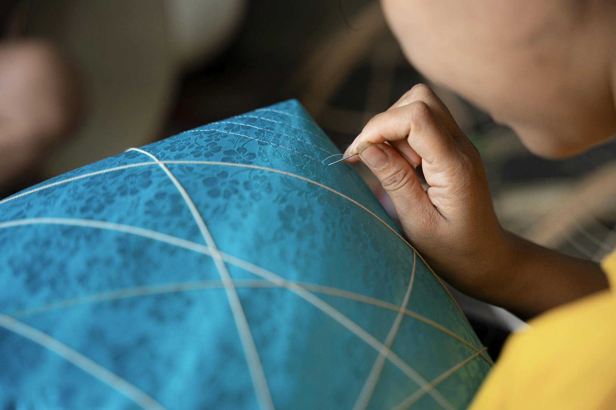 Close-up of a person sewing a vibrant blue traditional Vietnamese kite in Hà Nội.
